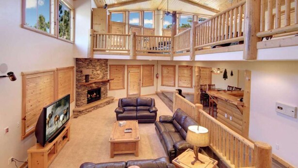 A spacious living area with a fireplace, leather sofas, a TV, and a balcony with wooden railings. - Starlight Retreat by Avantstay Gorgeous Log Style Home w Incredible Views (Big Bear Lake)