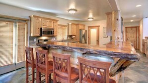 A kitchen with wooden cabinets, a granite countertop, and a central island with bar stools. - Starlight Retreat by Avantstay Gorgeous Log Style Home w Incredible Views (Big Bear Lake)