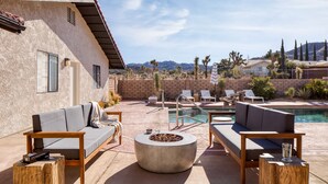 A poolside area with a stone wall, two sofas, a fire pit, and a pool. - Lava Rocks by Avantstay Gorgeous Desert Haven w Pool Hot Tub Fire Pit Ping Pong (Yucca Valley)