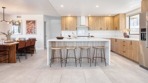 A modern kitchen with a central island, wooden cabinets, and bar stools. - Lava Rocks by Avantstay Gorgeous Desert Haven w Pool Hot Tub Fire Pit Ping Pong (Yucca Valley)