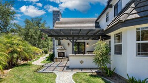 Une maison avec une cheminée en pierre, un patio couvert et un chemin menant à l’entrée.