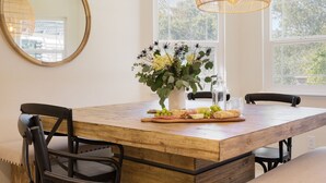 Un coin repas avec une table en bois, des chaises, un vase rempli de fleurs et un luminaire suspendu.