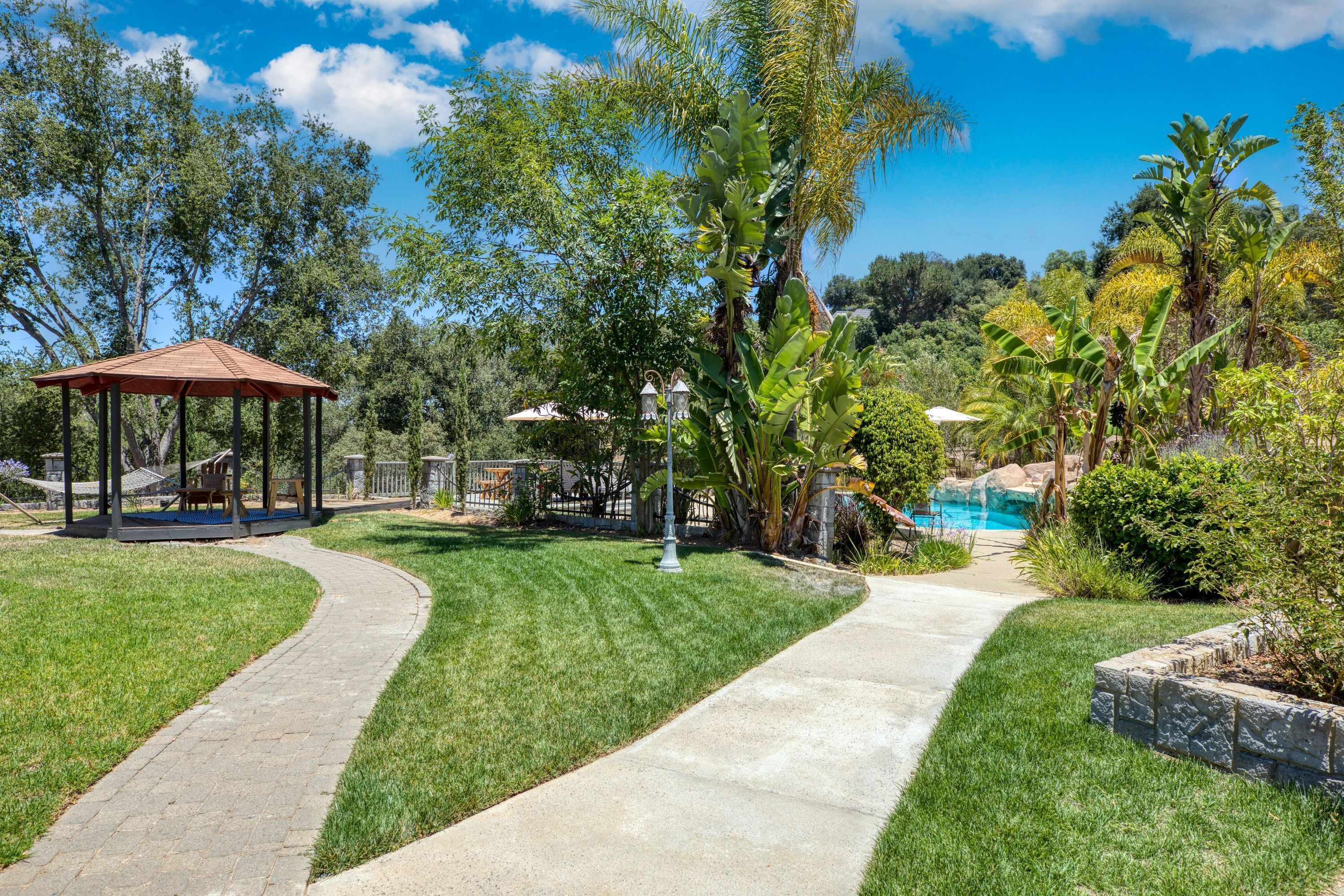 A garden with a gazebo, a winding concrete path, and a swimming pool.