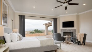 A bedroom with a large bed, a TV mounted on the wall, a fireplace, and a view of the outdoors. - Malbec by Avantstay Incredible Estate w Panoramic Views Bocce Ball Court (Temecula)
