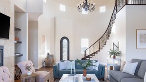 A spacious living room with a fireplace, a staircase, and a chandelier.