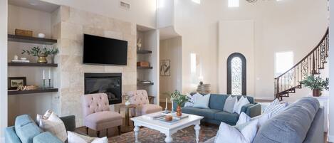 Un salón amplio con chimenea, televisor y una escalera que sube a otro nivel.
