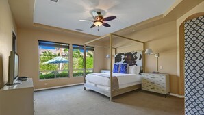 Camera da letto con letto a baldacchino, ventilatore a soffitto, scrivania con sedia e una grande finestra vista su del verde.