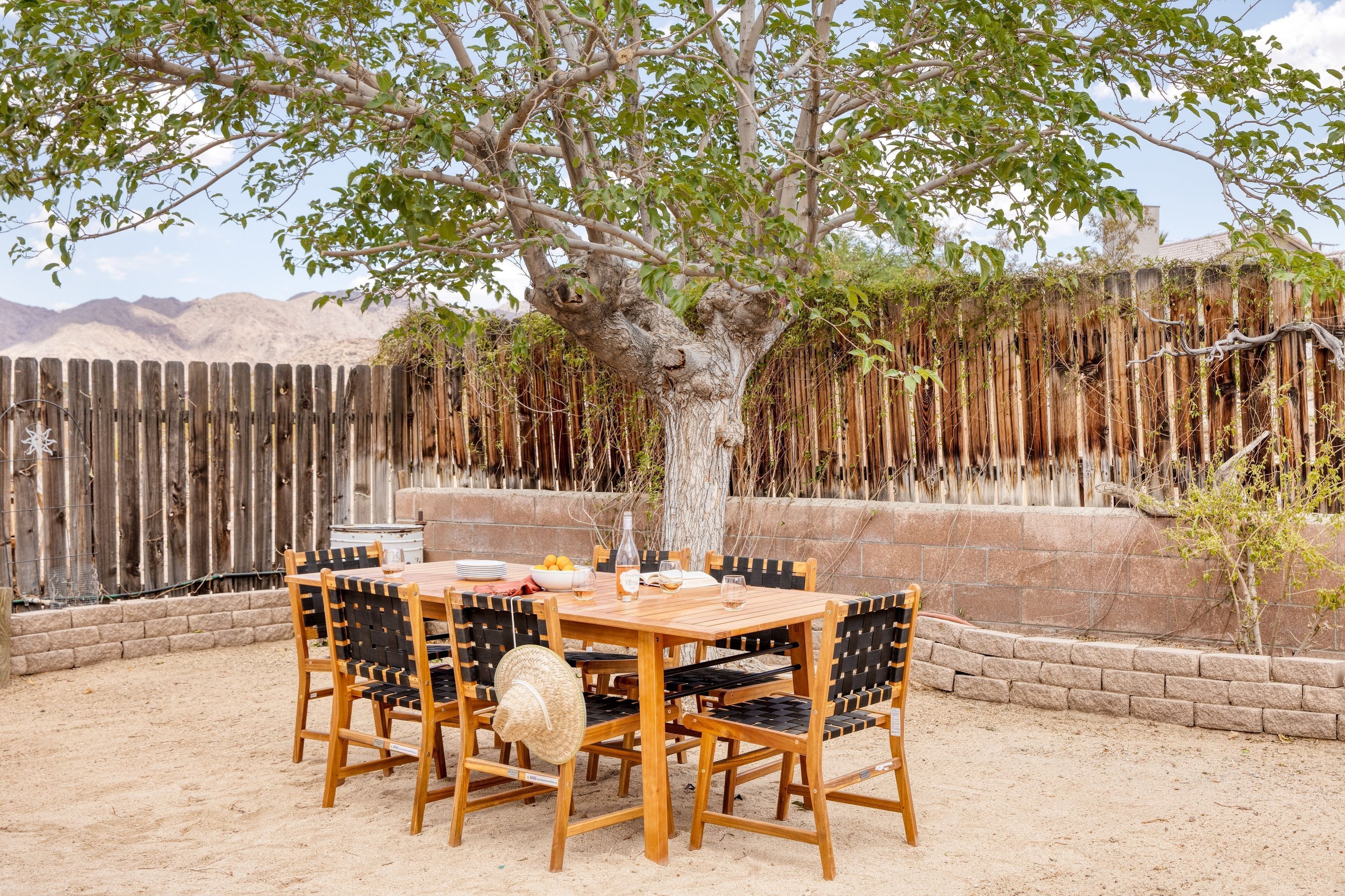 A wooden table and chairs set outdoors with a tree in the background.