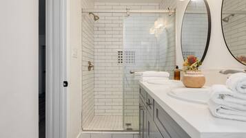 A modern bathroom with a walk-in shower, a large mirror, and a vanity with a sink and towel rack.