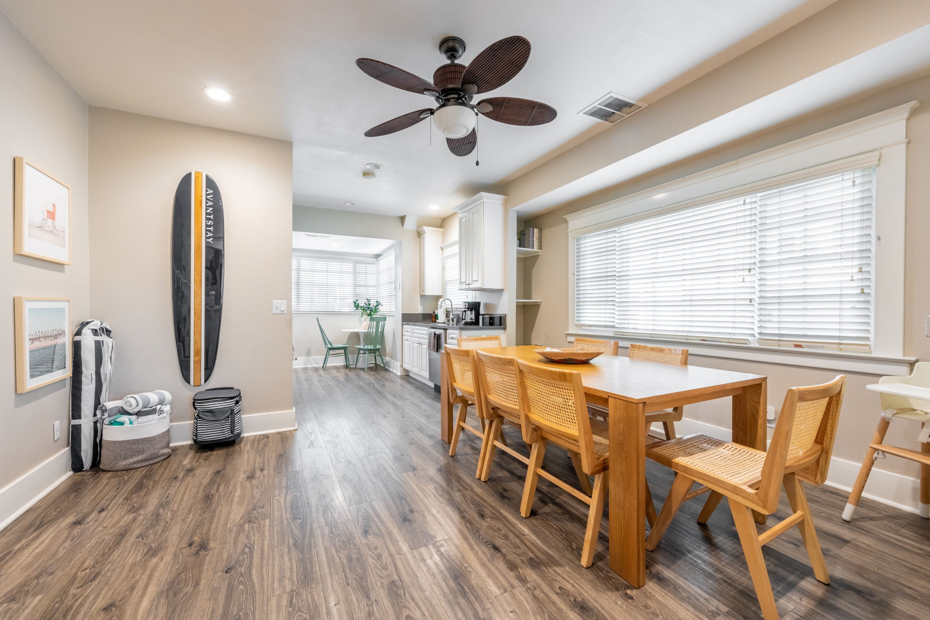 A modern kitchen with white cabinets, a dining area with wooden chairs, and a ceiling fan.