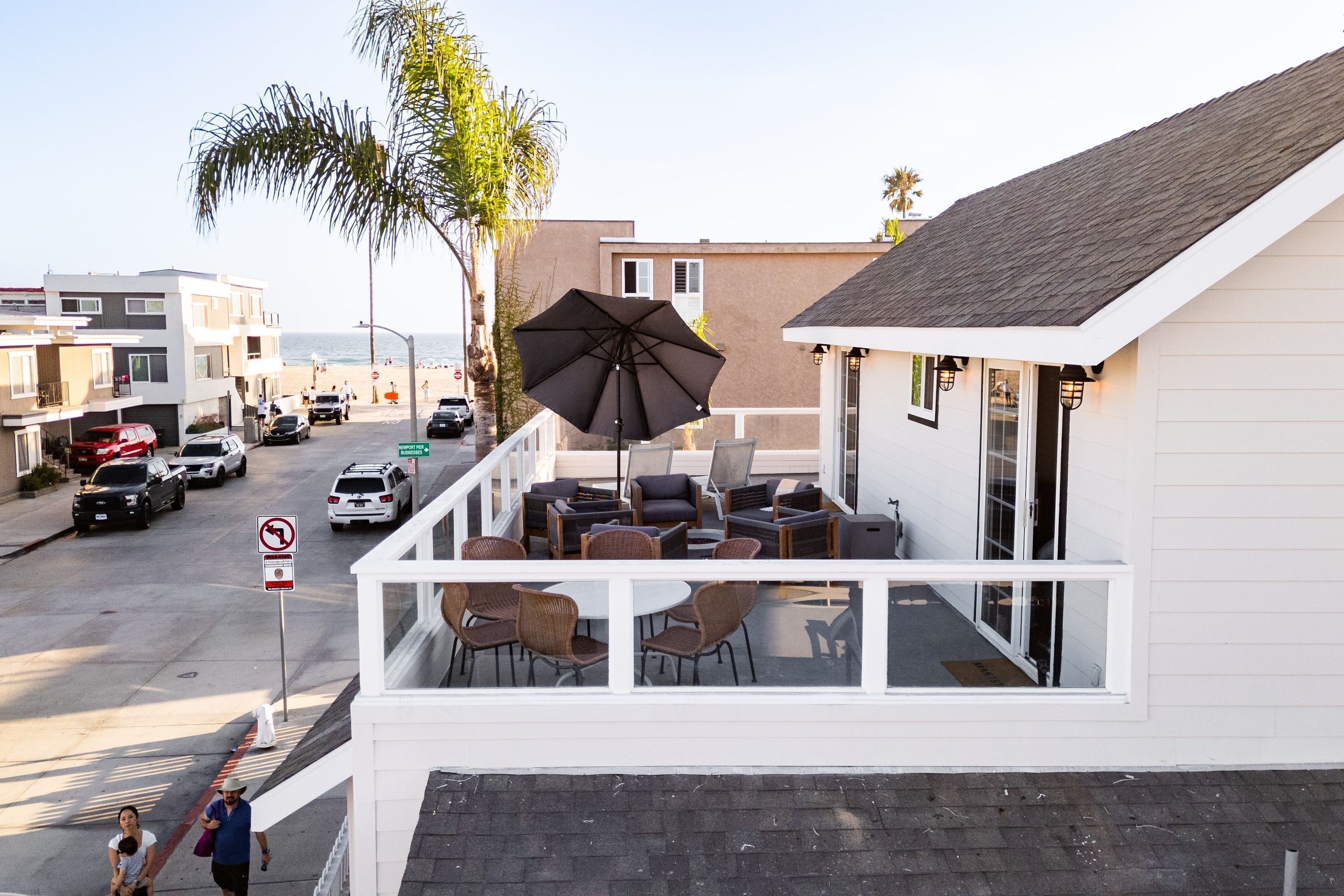 A balcony with outdoor seating, overlooking a street with parked cars and a beach in the background.