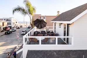 A balcony with outdoor seating, overlooking a street with parked cars and a beach in the background. - Sea Sight by Avantstay Walk to Newport Beach (Newport Beach)