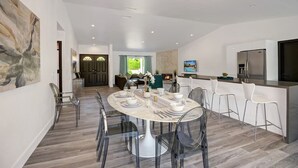 A modern kitchen with a large island, a dining area with a round table, and a living space with a fireplace. - Catalina by Avantstay Fully Remodeled Palm Springs Haven Pool Permit 3432 (Palm Springs)