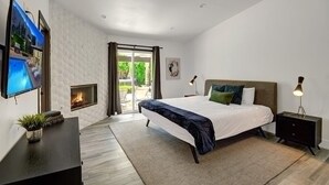 A modern bedroom with a large bed, a flat-screen TV, a fireplace, and a view of the outdoors. - Catalina by Avantstay Fully Remodeled Palm Springs Haven Pool Permit 3432 (Palm Springs)