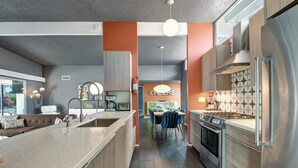 A modern kitchen with a central island, stainless steel appliances, and a dining area with blue chairs. - Biskra by Avantstay Classic Palm Springs Getaway W Outdoor Living Pool Permit 4869 (Palm Springs)