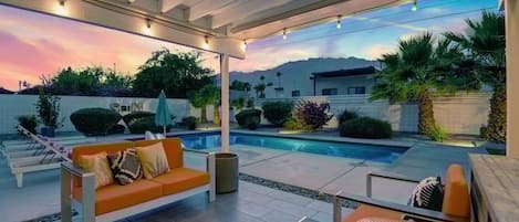 A covered outdoor area with a pool, orange seating, and a view of mountains.