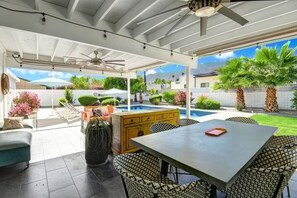 Eine überdachte Terrasse mit Pool, Gartenmöbeln und Deckenventilator.
