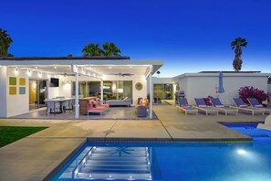 Una casa moderna con piscina, mobiliario exterior y un patio cubierto.