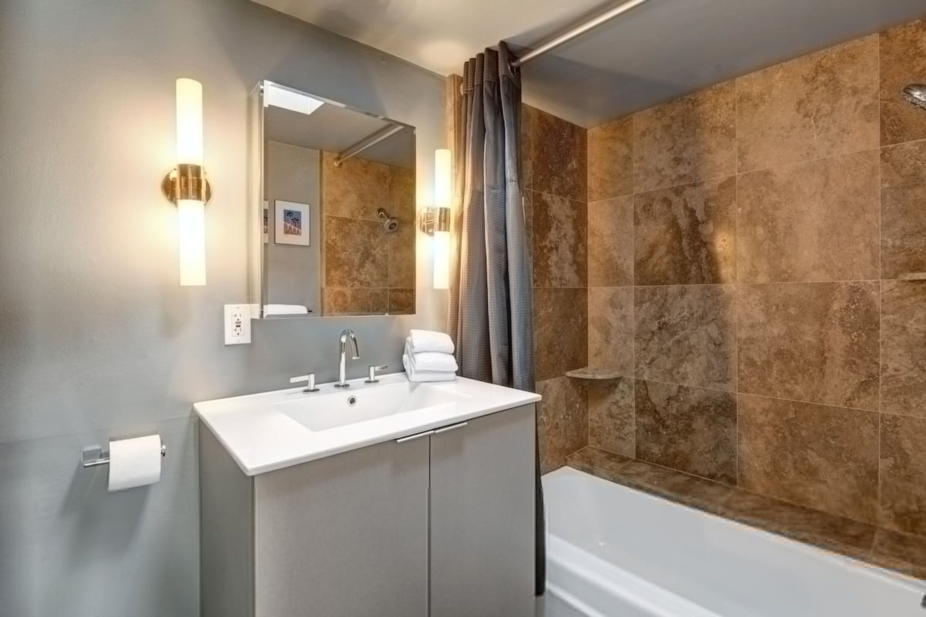 A modern bathroom with a white sink, two faucets, a mirror, and a shower area with a curtain.