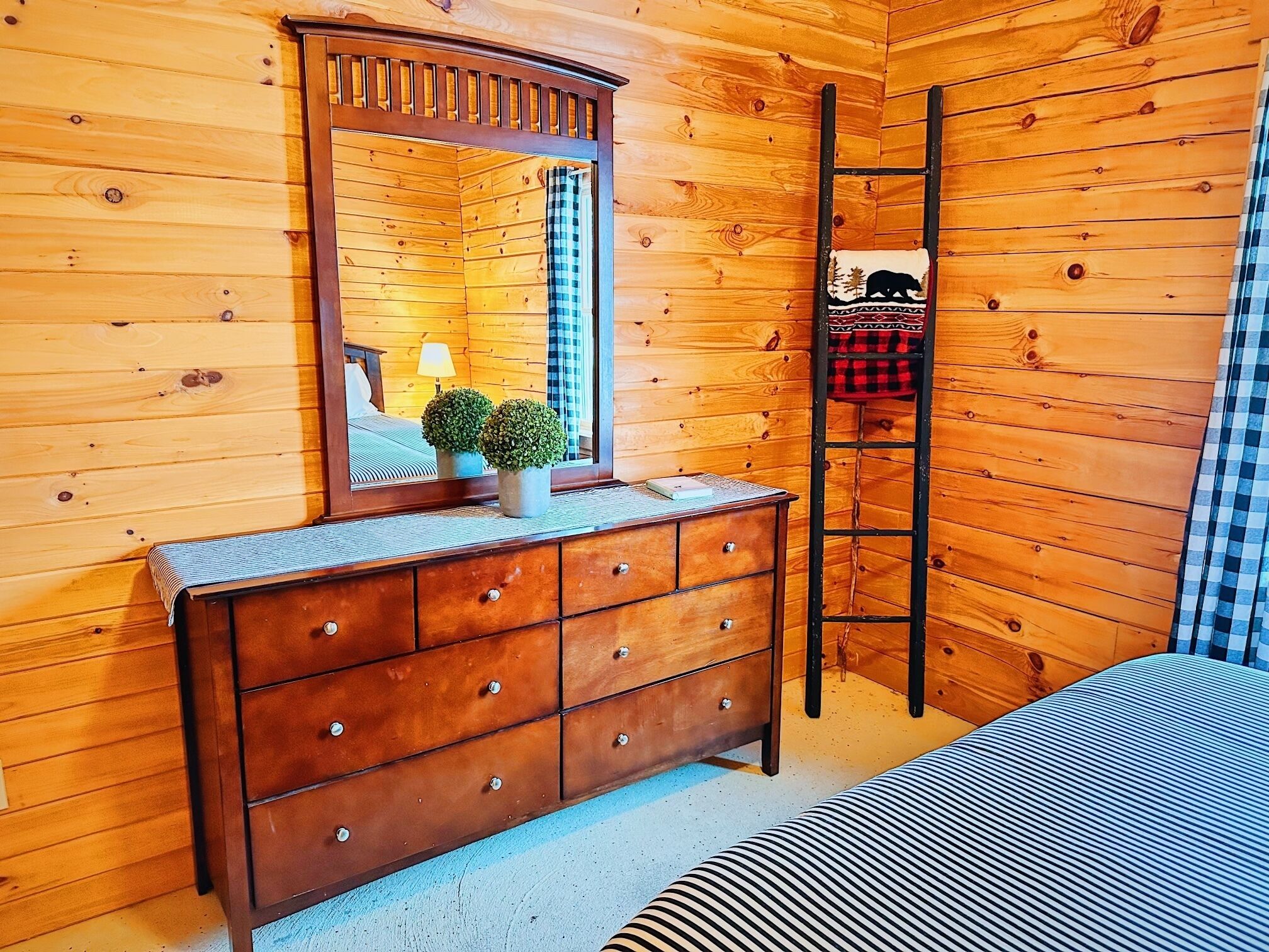 Une pièce de cabane en bois comprenant une commode, un miroir, une échelle et un lit.