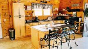 A cozy cabin-style kitchen with wooden walls and a central island with bar stools. - Cozy 2-bedroom cabin in welcoming Sangerville with WiFi (Sangerville)