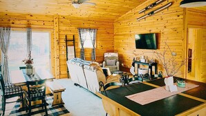 A cozy cabin interior with a wooden interior, a dining area with checkered tablecloths, a sofa, and a television mounted on the wall. - Cozy 2-bedroom cabin in welcoming Sangerville with WiFi (Sangerville)