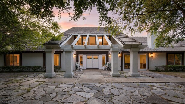 A stone-paved entrance with a covered walkway, columns, and a building with large windows and doors. - Quarter Horse by Avantstay Countryside Retreat (Temecula)