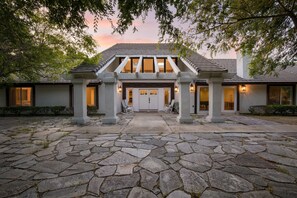 A stone-paved entrance with a covered walkway, columns, and a building with large windows and doors. - Quarter Horse by Avantstay Countryside Retreat (Temecula)