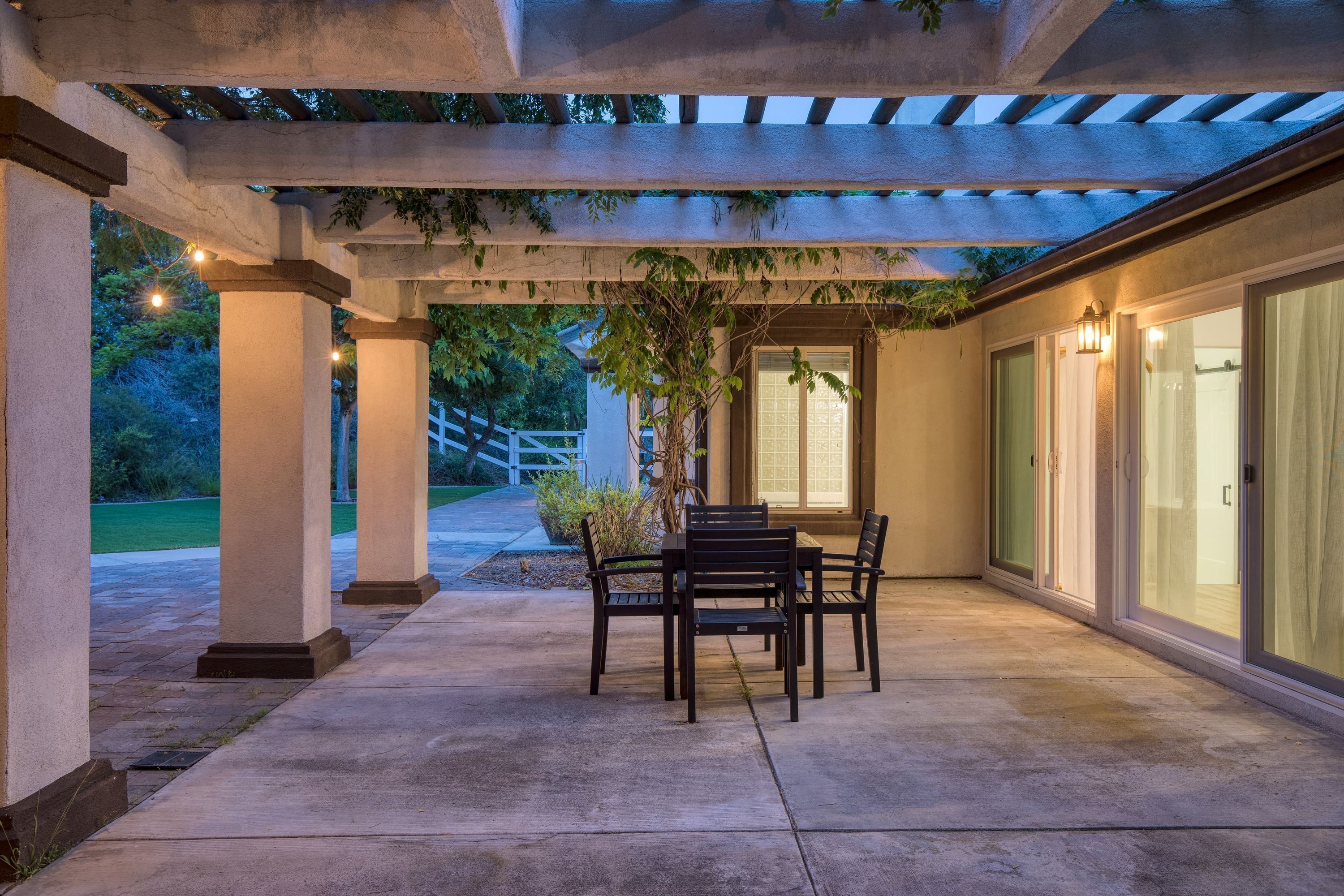 A covered patio area with a table and chairs, columns, and a pergola with string lights.