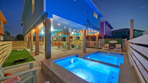 Un área de piscina con un jacuzzi, terraza de madera y sillas de descanso.