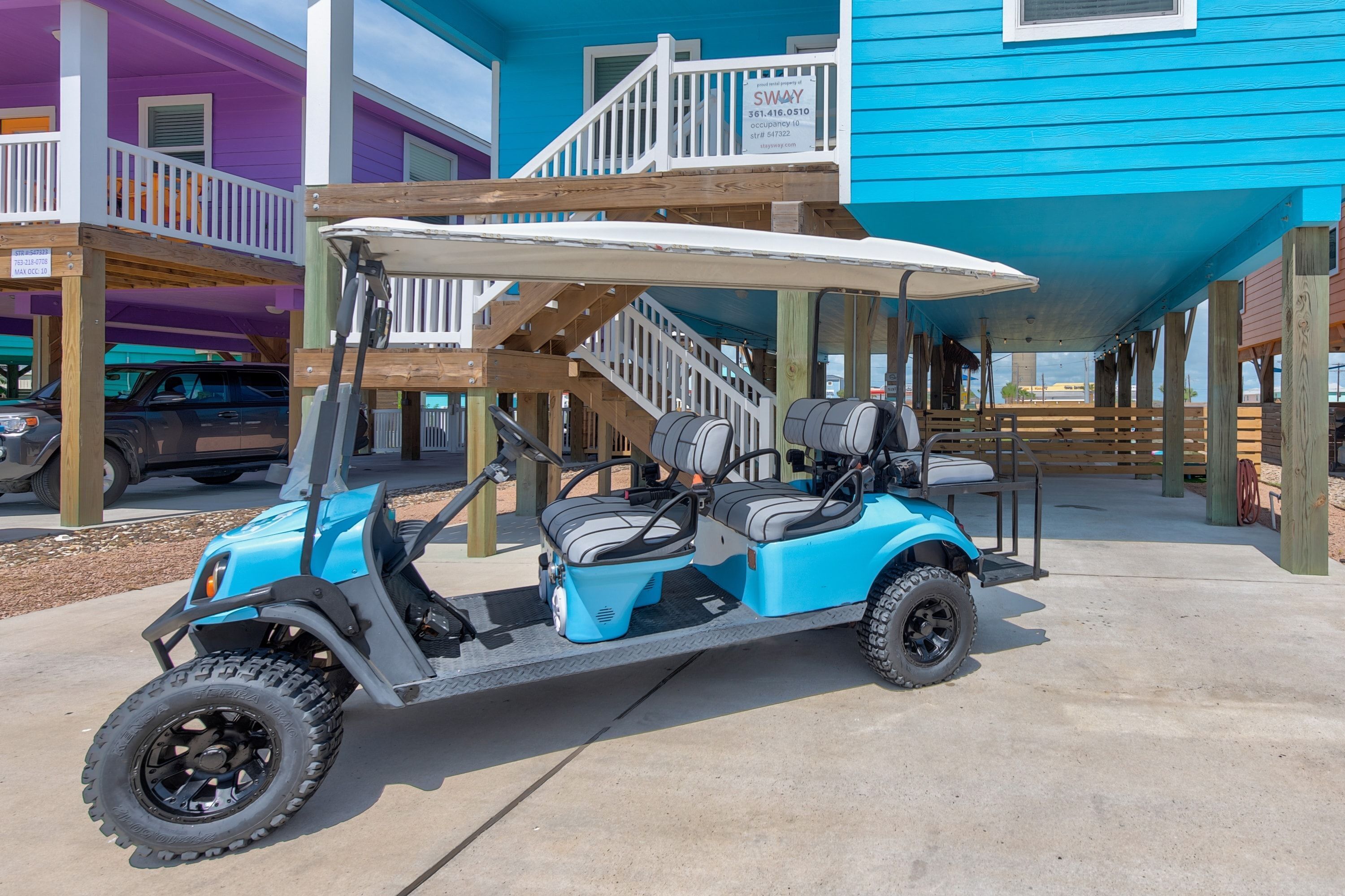 A blue golf cart parked on a concrete surface in front of a building with a blue exterior and a white balcony.