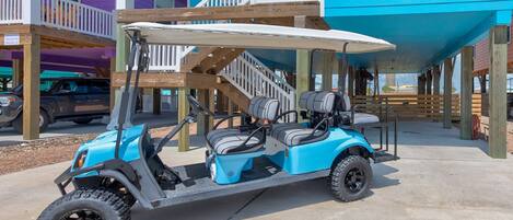 A blue golf cart parked on a concrete surface in front of a building with a blue exterior and a white balcony.