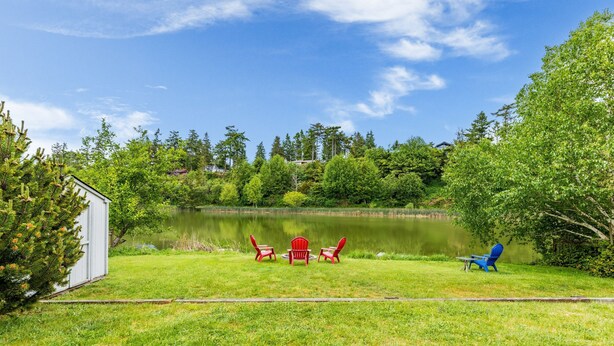 A lakeside view with a grassy area, a small shed, and two red Adirondack chairs facing the water. - Beach Lookout Retreat by Avantstay Rooftop Views (Coupeville)