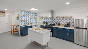 A modern kitchen with blue cabinets, a white island, and a stainless steel refrigerator. - Fable by Avantstay 2 Unique Spaces w Bowling Hot Tub Fire Pit Large Yard (Joshua Tree)