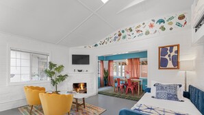 A modern living room with a fireplace, yellow chairs, a blue sofa, and a colorful wall mural. - Fable by Avantstay 2 Unique Spaces w Bowling Hot Tub Fire Pit Large Yard (Joshua Tree)