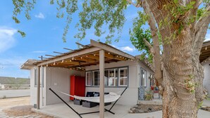 A modern house with a covered porch, a hammock, and a large tree. - Fable by Avantstay 2 Unique Spaces w Bowling Hot Tub Fire Pit Large Yard (Joshua Tree)