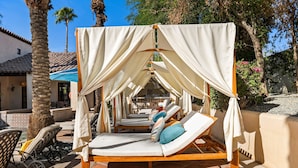 A sunbed with a canopy, surrounded by palm trees and a tiled patio.