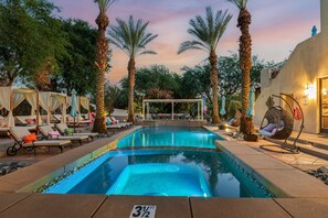 A swimming pool with lounge chairs and umbrellas, surrounded by palm trees and a building with a balcony. - Villa del Gallo by Avantstay Luxury Group Retreat Pool Putting Green (Indio)