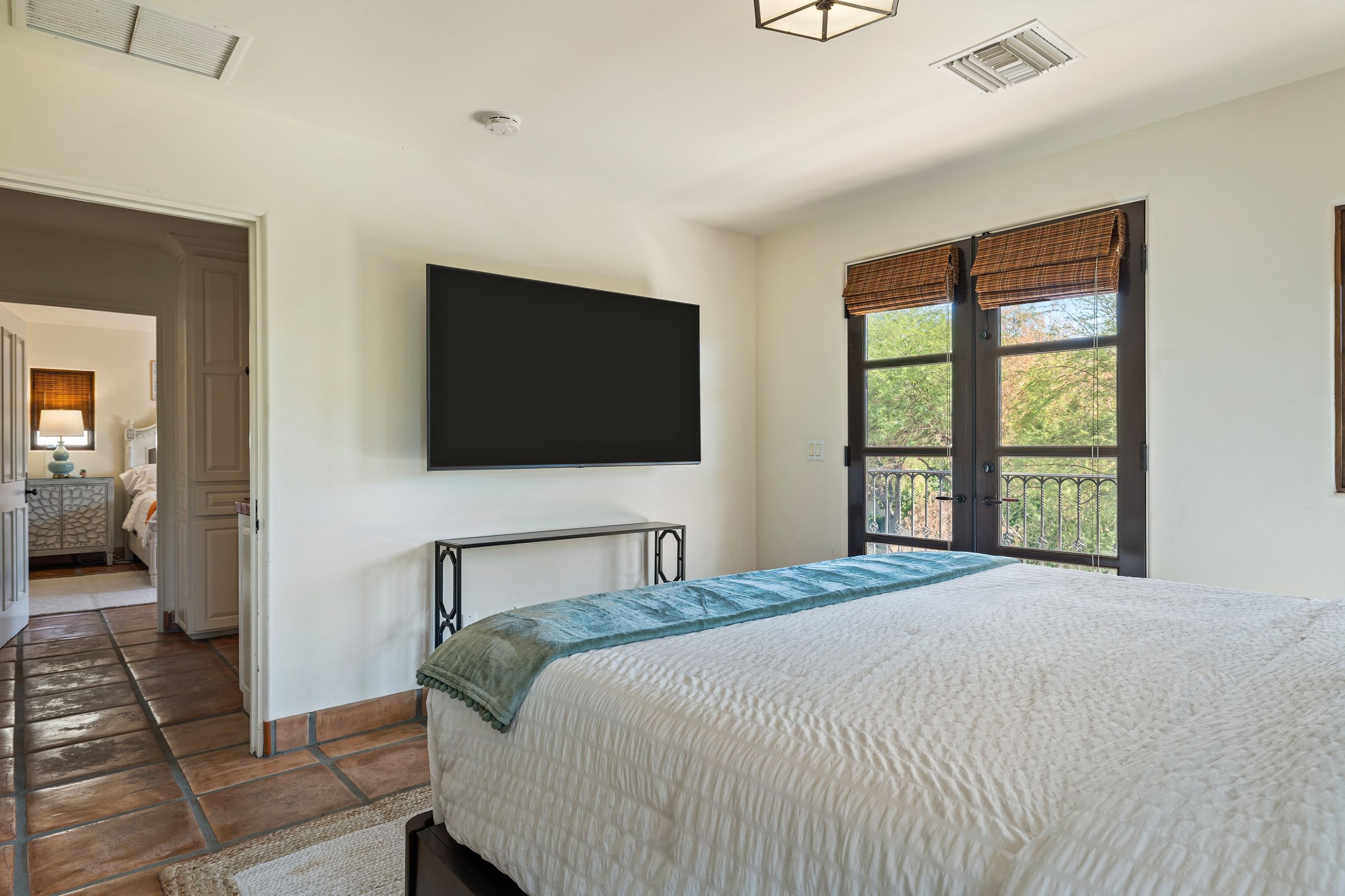 Un dormitorio con una cama grande, un televisor montado en la pared y una ventana con persianas.