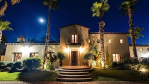 A two-story building with a balcony, surrounded by palm trees and well-lit by street lamps.