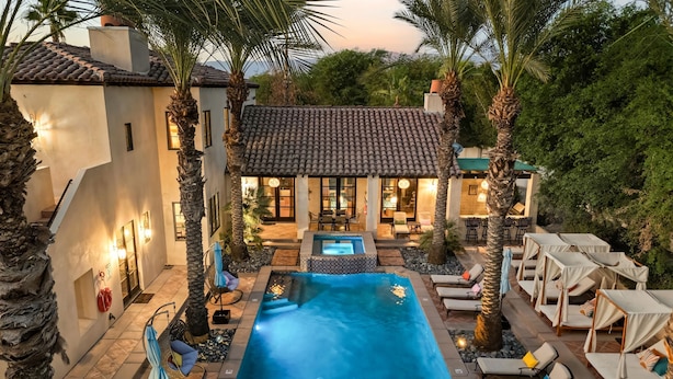 A pool area with lounge chairs, a hot tub, and a patio with umbrellas.