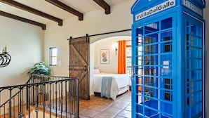 A room with a bed, a blue telephone booth, and a wooden door.