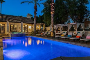 An outdoor swimming pool with lounge chairs and umbrellas, surrounded by palm trees and a building with a tiled roof. - Villa del Gallo by Avantstay Luxury Group Retreat Pool Putting Green (Indio)