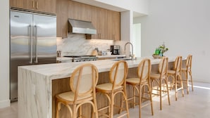 A modern kitchen with a large island, stainless steel refrigerator, wooden cabinets, and a marble countertop. - The Reserve at Polo Villas 15 by Avantstay (La Quinta)