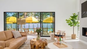 A modern living room with a beige sofa, a wooden coffee table, and a glass door leading to a balcony with yellow umbrellas. - The Reserve at Polo Villas 15 by Avantstay (La Quinta)