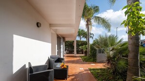 A covered outdoor seating area with wicker furniture and a fruit tray, surrounded by palm trees and greenery. - Villetta Sea Breeze (Melendugno)
