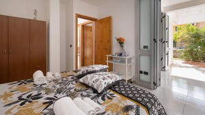 A bedroom with a bed, wooden wardrobe, a white shelf with a vase, and a sliding glass door leading to an outdoor area. - Villetta Sea Breeze (Melendugno)