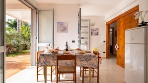 A dining area with a table set for two, a refrigerator, and a sliding glass door leading to a garden. - Villetta Sea Breeze (Melendugno)
