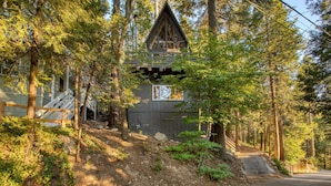 A cabin with a steep wooden staircase leading to a door, surrounded by dense forest. - A-frame Retreat by Avantstay Modern Interiors 2 Decks Views (Skyforest)