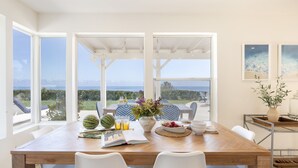 A dining area with a wooden table, white chairs, and a view of the sea. - Stardust by Avantstay Views Hot Tub Pool Table (Malibu)